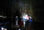 The group light the cave as someone enters from left